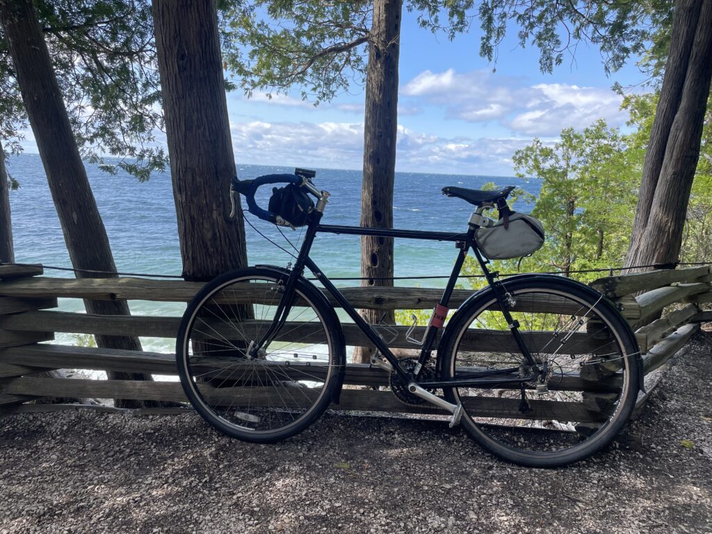 Greg’s Surly Long Haul Trucker bike parked against a log fence. In the background, Green Bay looking west lies through the trees.