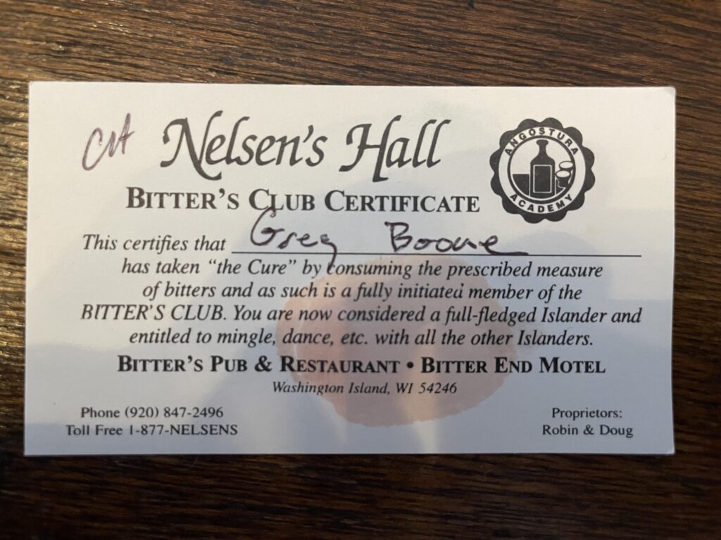 A business card sized piece of paper stamped with a pink thumbprint from Nelsen’s Hall. It reads: “This certifies that Greg Boone has taken ‘the Cure’ by consuming the prescribed measure of bitters and as such is a fully initiated member of the Bitters Club. You are now considered a full-fledged Islander and entitled to mingle, dance, etc. with all the other Islanders.”